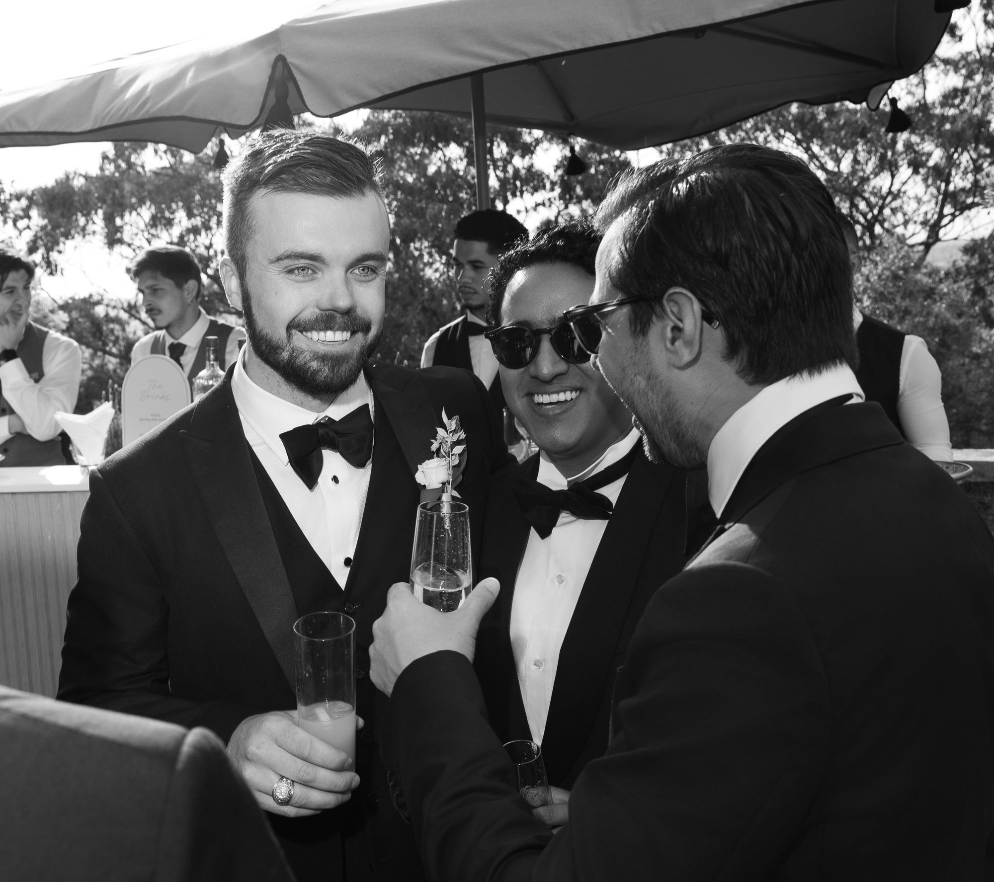 Groom and guests in black tie laughing together with drinks